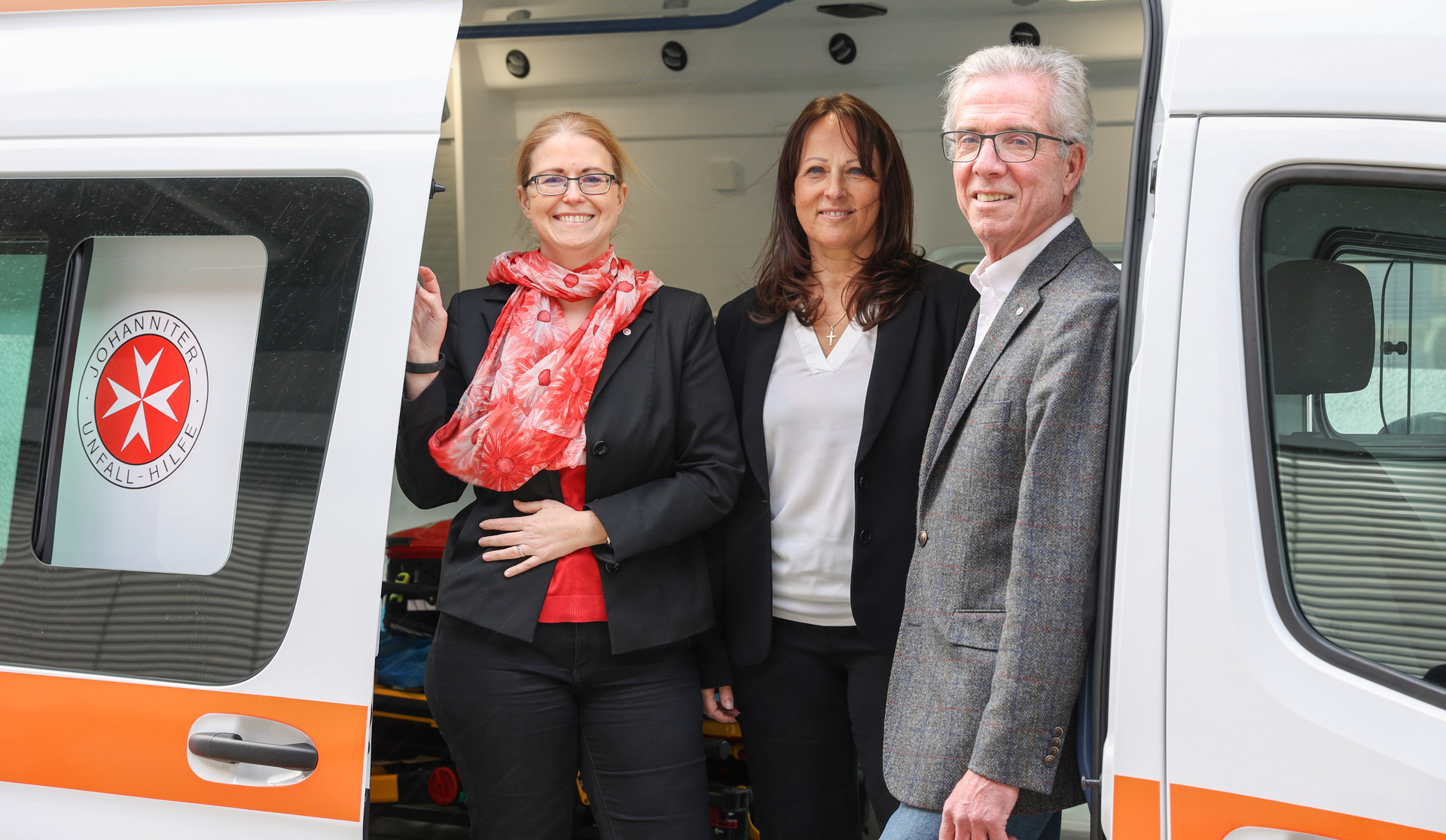 Bundesgeschäftsführerin Petra Grell-Kunzinger, Geschäftsführerin Wien-NÖ Karin Zeiler-Fidler und Johanniter Präsident Johannes Bucher stehen in einem Krankenwagen.