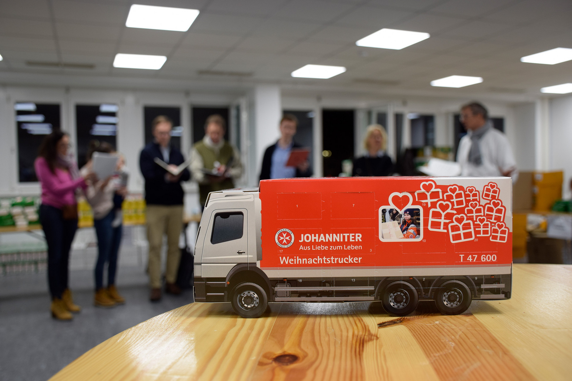 Ein Weihnachtstrucker-Adventkalender - im Hintergrund stehen 7 Leutem die singen.