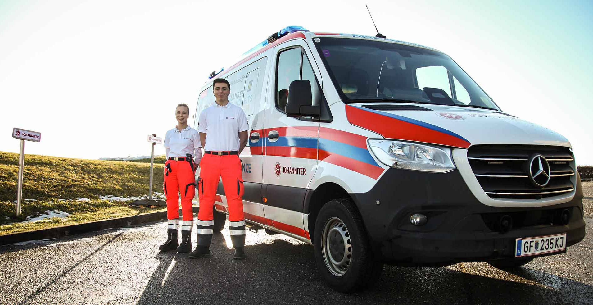 Ein Team von zwei Johannitern steht neben einem Einsatzauto der Johanniter.