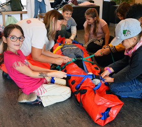 Schüler:innen helfen einer Johanniterin beim Anlegen einer Vakuum-Matratze.
