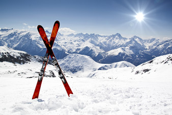 zwei gekreuzte rote Schi stecken im Schnee, im Hintergrund sieht man verschneite Berge