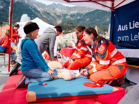 Eine Johanniterin erklärt einem Mädchen die Reanimation an einem Säugling.