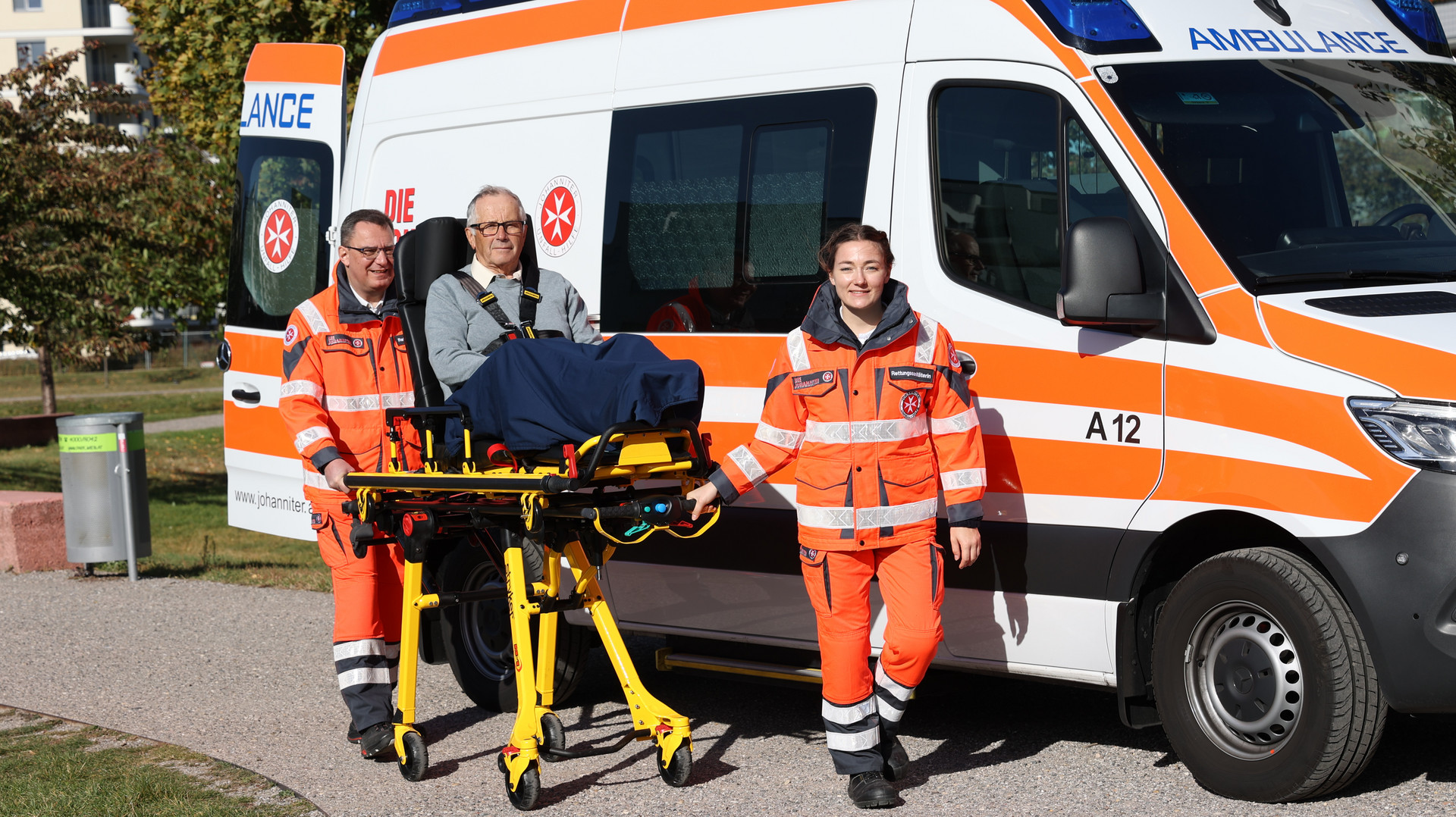 Zwei Johanniter befördern einen Patienten auf einer Fahrtrage am Krankenwagen vorbei.