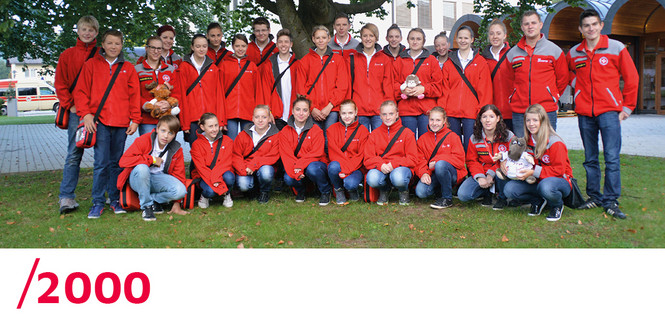 2000: Ein Gruppenfoto der Johanniter-Jugend: Alle tragen eine rote Jacke und eine Umhängetasche der Johanniter.