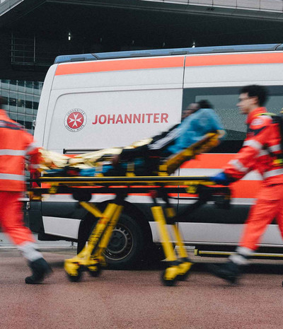 Zwei Zivis schieben einen Patienten auf einer Trage zum Krankenwagen.