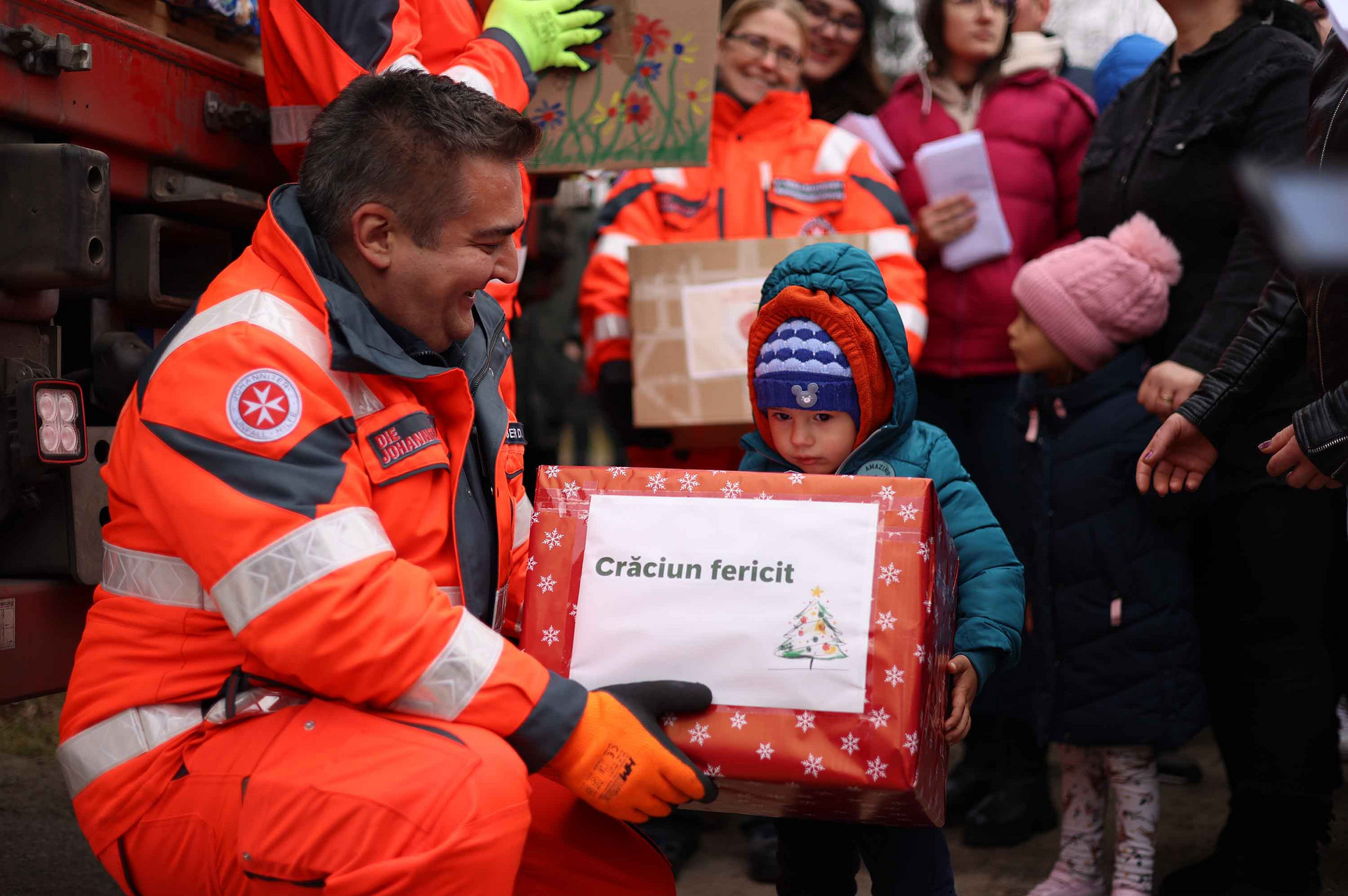 Ein Johanniter übergibt einem Kind das Paket des Weihnachtstruckers.