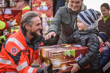 Ein Johanniter übergibt einem kleinen Jungen ein Geschenkspaket vom Weihnachtstrucker.