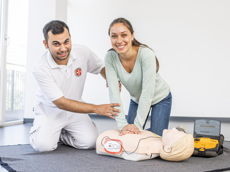 Eine Frau übt unter Anleitung des Kursleiters die Wiederbelebung mit Defibrillator an einer Puppe.