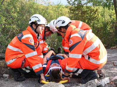 Vier Johannter knien bei der verletzten Patientin, um sie auf der Trage hochzuheben.