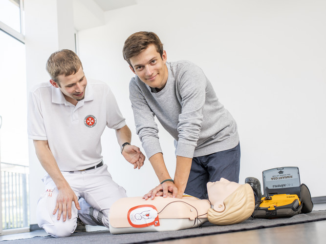 Ein Mann übt unter Anleitung des Kursleiters die Wiederbelebung mit Defibrillator an einer Puppe.