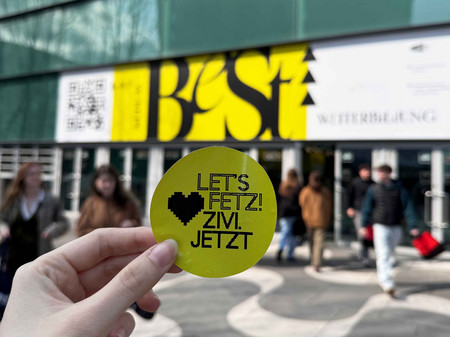 Ein "zivi.jetzt"-Sticker wird vor dem Eingang der Messe Wien hochgehalten.