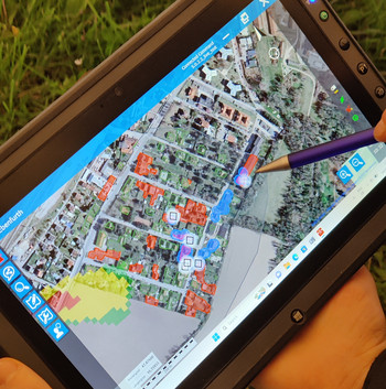 Auf einem Tablet ist eine Aufnahme von einem Ort zu sehen, wo manche Häuser rot markiert sind.