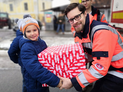 Ein Johanniter übergibt einem kleinen Jungen sein Geschenk vom Weihnachtstrucker.