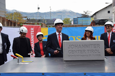 Der Präsident der Johanniter hält für traditionelle Hammerschläge einen Hammer in der Hand, er steht neben dem Grundstein des "Johanniter Center Tirol"