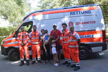 Eine Familie steht mit 4 Johannitern vor dem Rettungsauto.