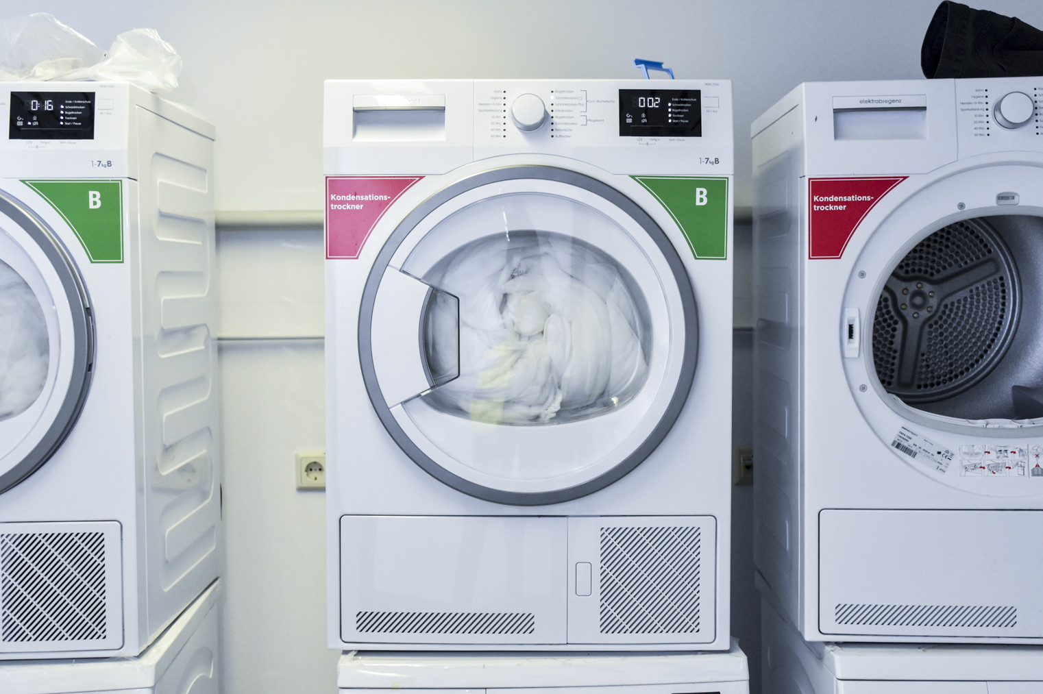 Nebeneinander stehen drei Trockner, die jeweils auf einer Waschmaschine stehen.