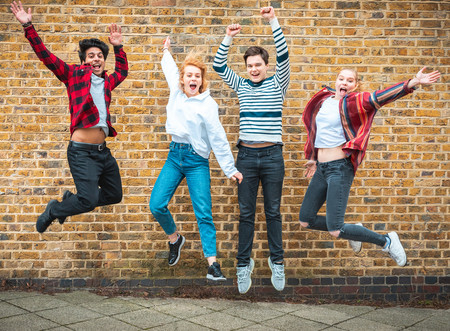 Vier Jugendliche springen vor einer braunen Ziegelhauswand in die Luft und strecken dabei die Hände hoch.