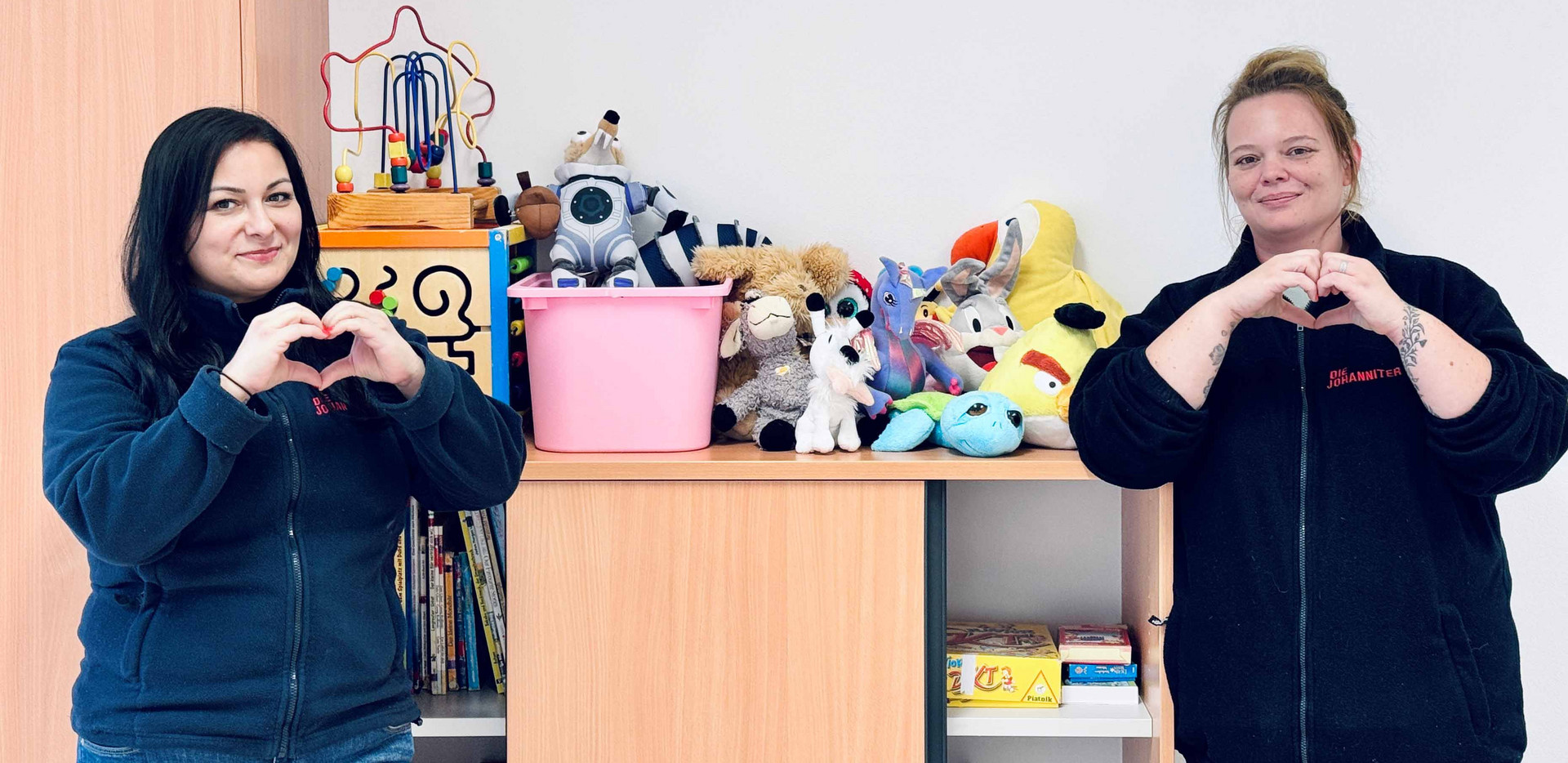 Zwei Betreuerinnen zeigen ein Herz in die Kamera, als Danke-Zeichen für die Spielzeugspenden
