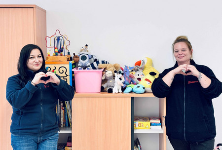 Zwei Betreuerinnen zeigen ein Herz in die Kamera, als Danke-Zeichen für die Spielzeugspenden