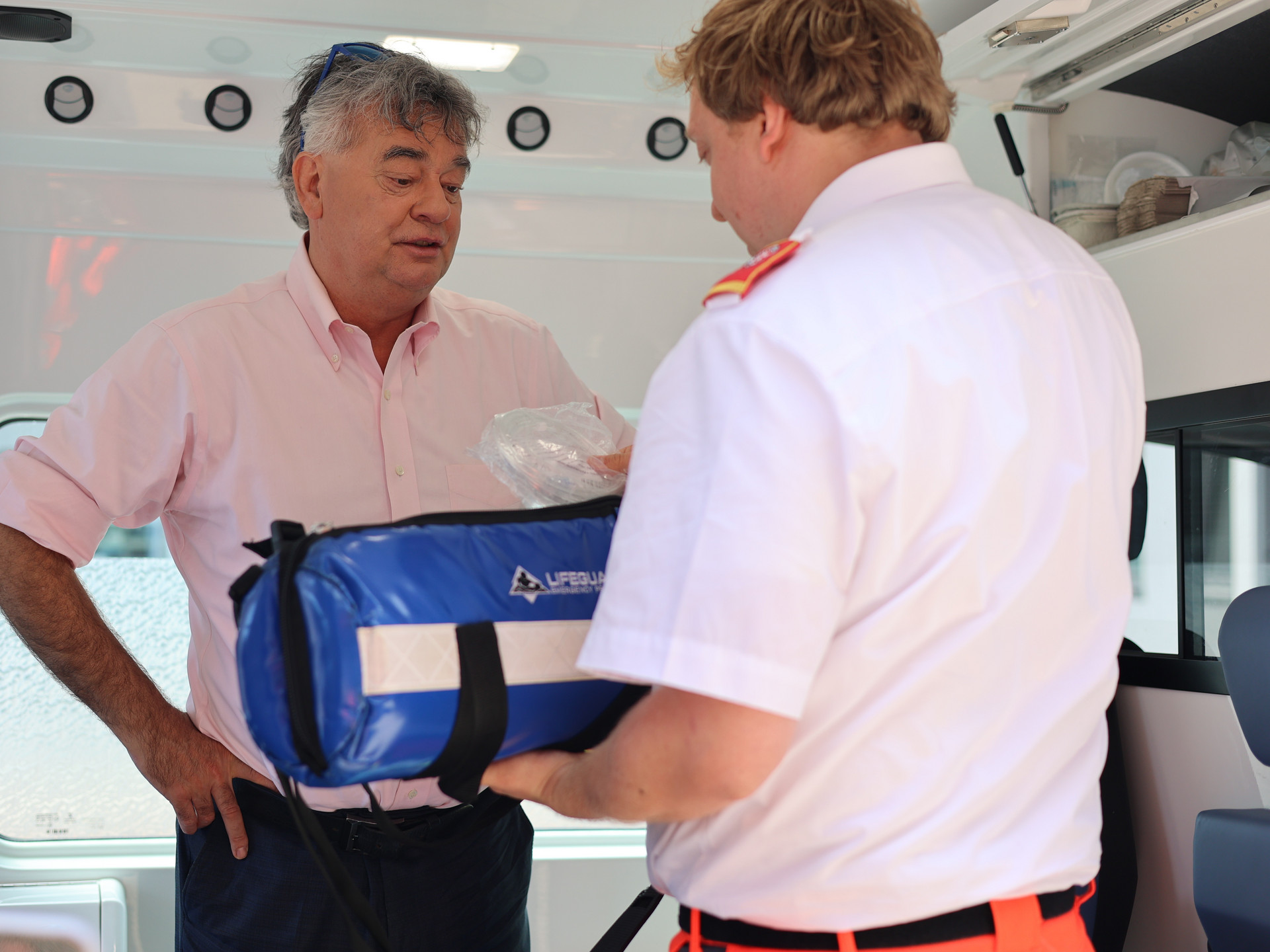 Ein Sanitäter in Uniform zeigt Werner Kogler Equipment aus dem Rettungswagen