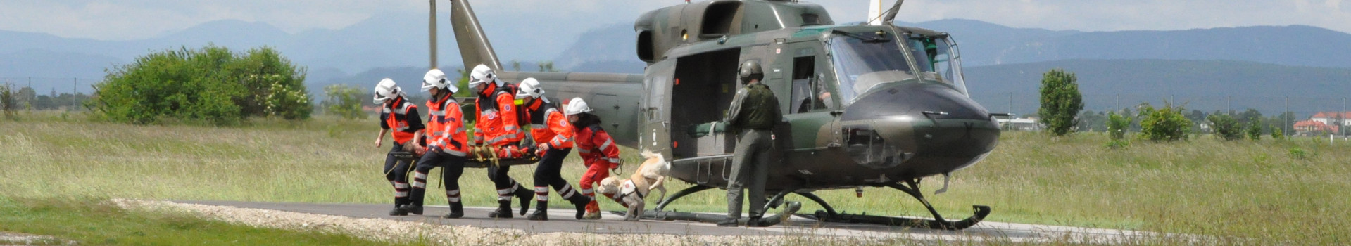 Bei einer Hubschrauberübung laufen fünf Johanniter und ein Rettungshund mit einer verletzten Person vom eben gelandeten Hubschrauber weg.