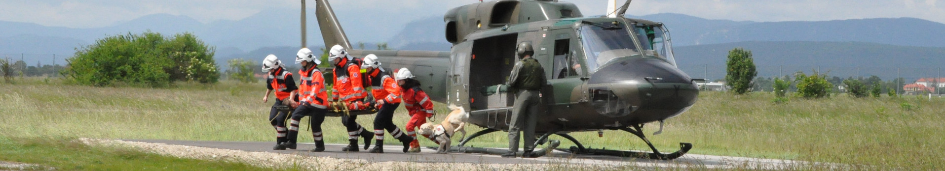 Bei einer Hubschrauberübung laufen fünf Johanniter und ein Rettungshund mit einer verletzten Person vom eben gelandeten Hubschrauber weg.