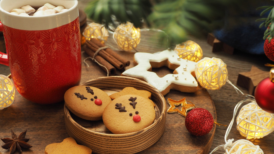 Heißgetränk und Kekse umgeben von weihnachtlicher Deko.