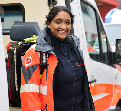 Myurri steigt lächelnd aus dem Rettungswagen. Sie trägt die orangene Johanniter-Uniform.