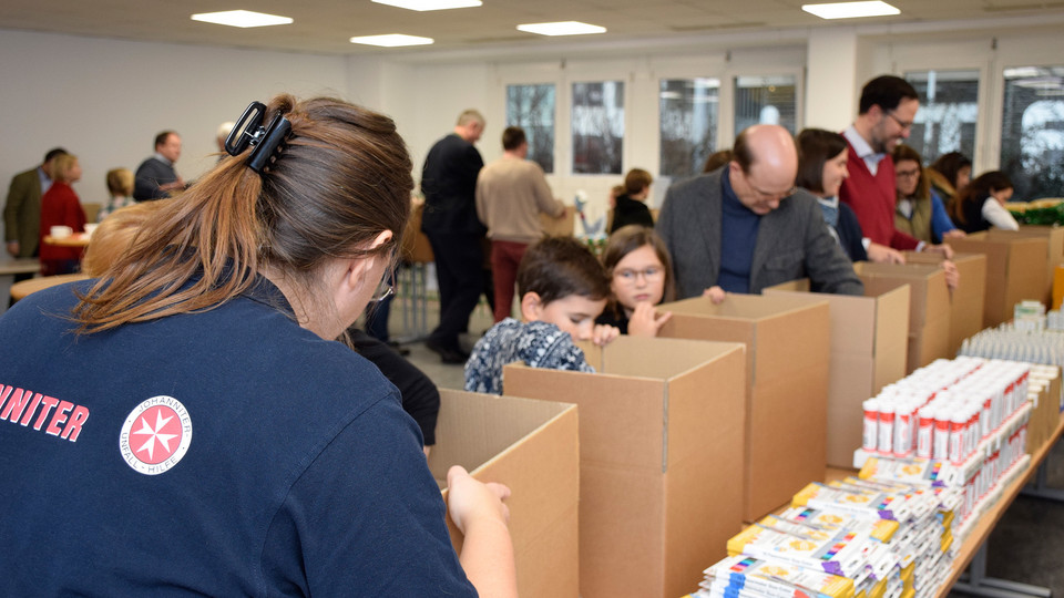 In Fließbandarbeit werden Hilfspakete mit Lebensmittel gefüllt.