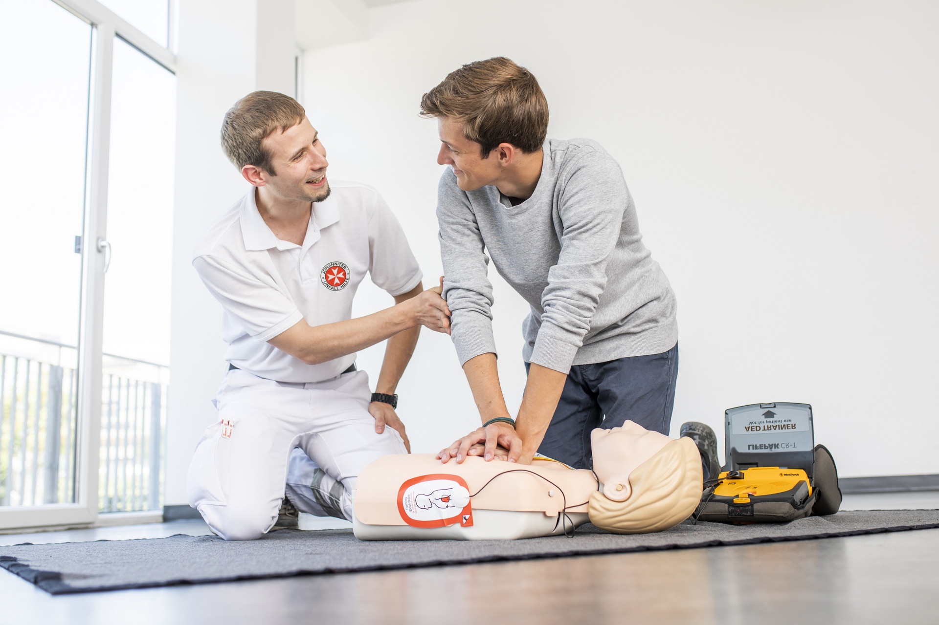 Ein Mann übt unter Anleitung des Kursleiters die Wiederbelebung mit Defibrillator an einer Puppe.