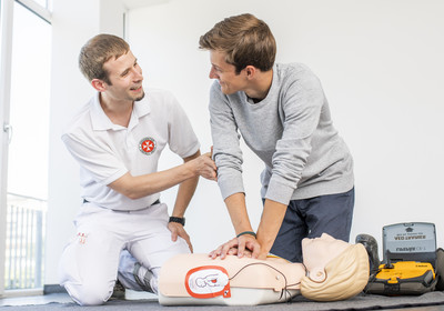 Ein Mann übt unter Anleitung des Kursleiters die Wiederbelebung mit Defibrillator an einer Puppe.