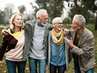 Vier glückliche Senior:innen gehen umarmt durch einen Park.