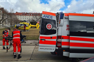 Zwei Sanitäter laden die Trage aus dem Auto aus. Im Hintergrund steht der Rettungshubschrauber.