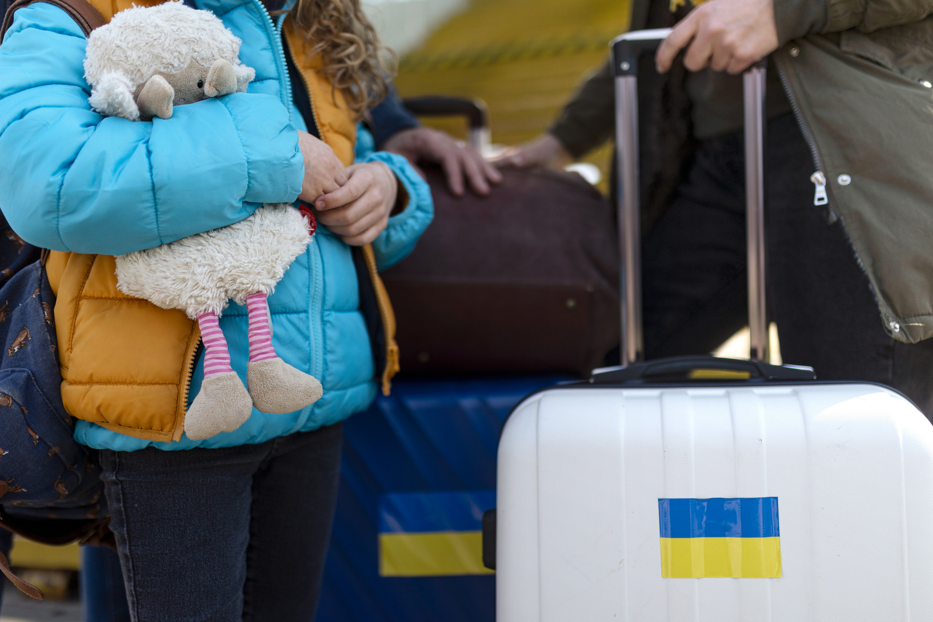 Ukrainische Flüchtlinge stehen mit Gepäck am Bahnhof. Das Mädchen hält ein Stofftier in der Hand.