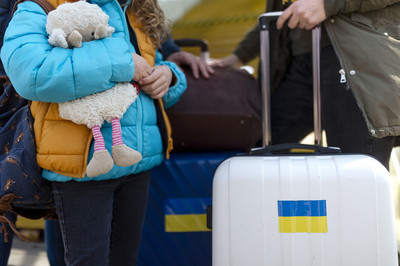 Ukrainische Flüchtlinge stehen mit Gepäck am Bahnhof. Das Mädchen hält ein Stofftier in der Hand.