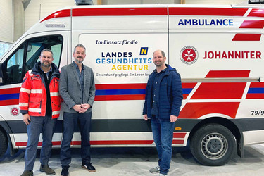 Der Bürgermeister von Spillern steht gemeinsam mit zwei Johannitern vor einem Johanniter-Rettungsauto.