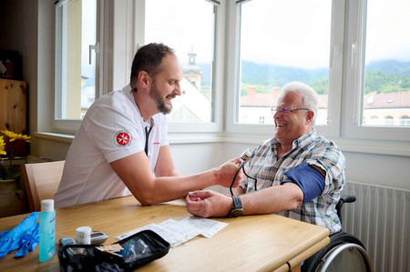 Ein Johanniter-Pfleger misst bei einem Hausbesuch bei einem Klienten den Blutdruck.