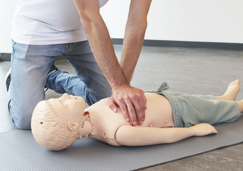 Ein Kursleiter zeigt die Herzdruckmassage am Kind mit einer Puppe.