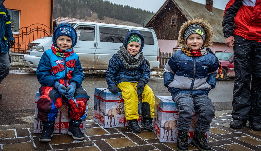 Drei Kinder sitzen auf Weihnachtstrucker-Paketen und lächeln in die Kamera.