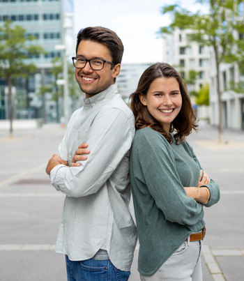 Zwei Ehrenamtliche stehen lachend mit verschränkten Armen Rücken an Rücken.