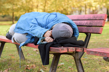 Eine Wohnungslose schläft auf einer Parkbank.