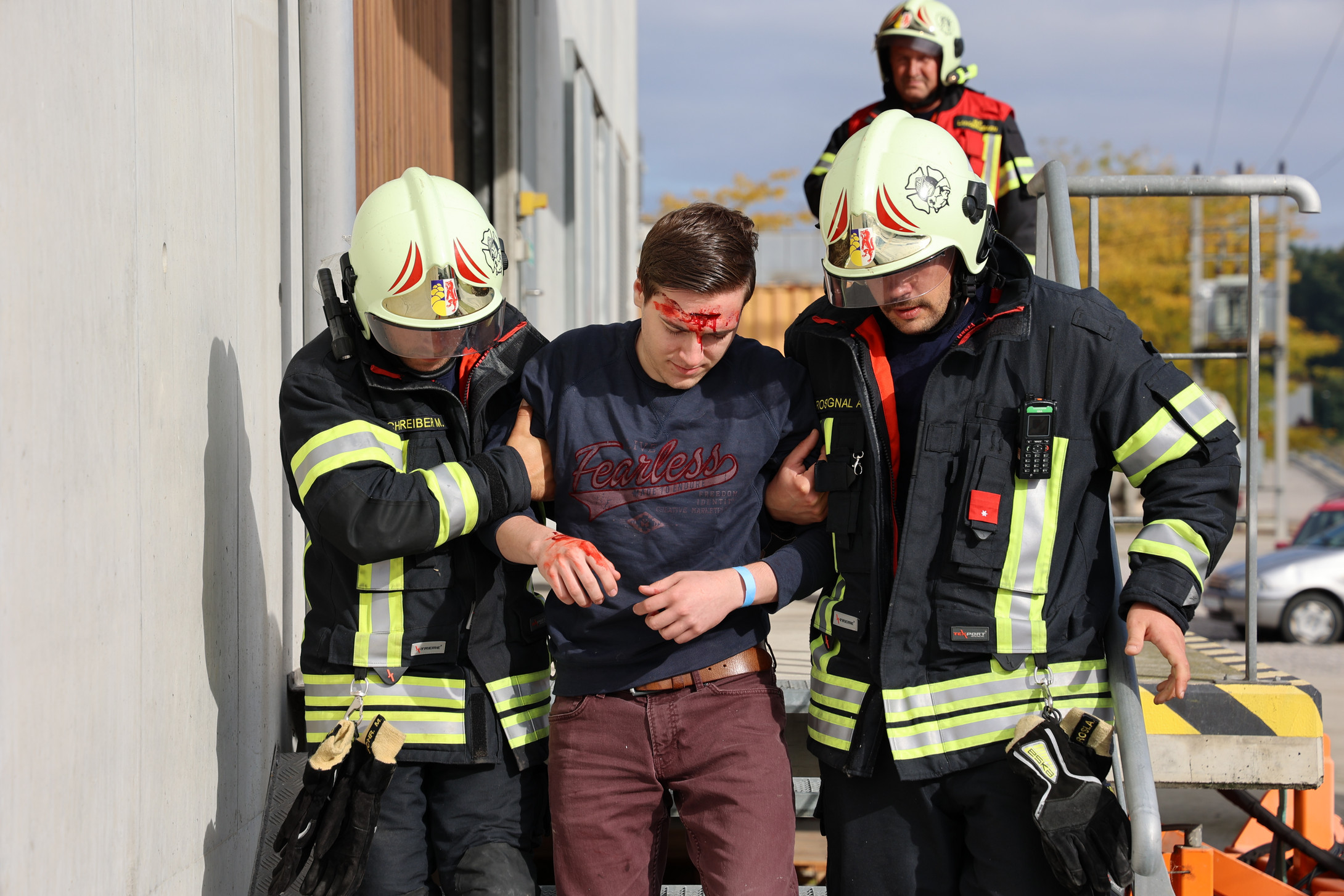 Zwei Feuerwehrleute stützen einen Patienten, der eine Schnittverletzung an der Stirn hat, beim Runtergehen einer Stiege.