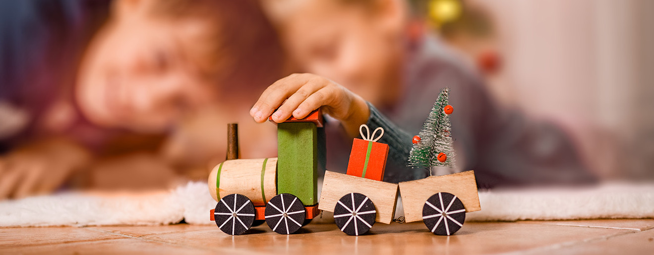 Zwei Kinder spielen an Weihnachten mit einem Spielzeugzug vor dem Christbaum.
