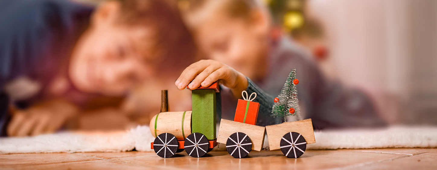 Zwei Kinder spielen an Weihnachten mit einem Spielzeugzug vor dem Christbaum.