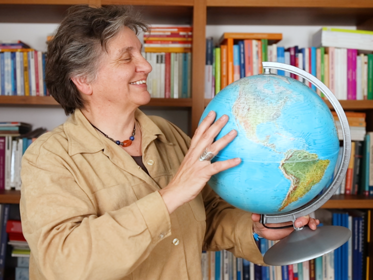 Eine Frau, Barbara, steht vor einem Bücherregal und hat einen Globus in der Hand.