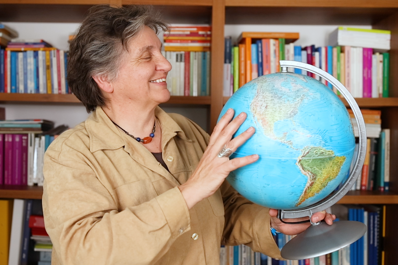 Eine Frau, Barbara, steht vor einem Bücherregal und hat einen Globus in der Hand.