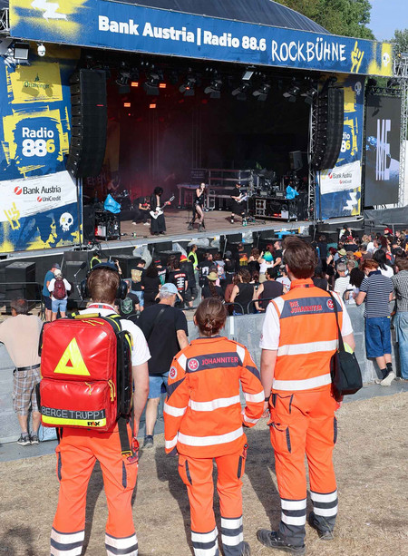 Drei Johanniter schauen beim Donauinselfest auf die Rock-Bühne, wo sie den Ambulanzdienst betreuen.