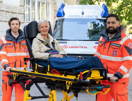 Zwei Zivildienstleistende, die eine Fahrtrage mit einer Patientin schieben