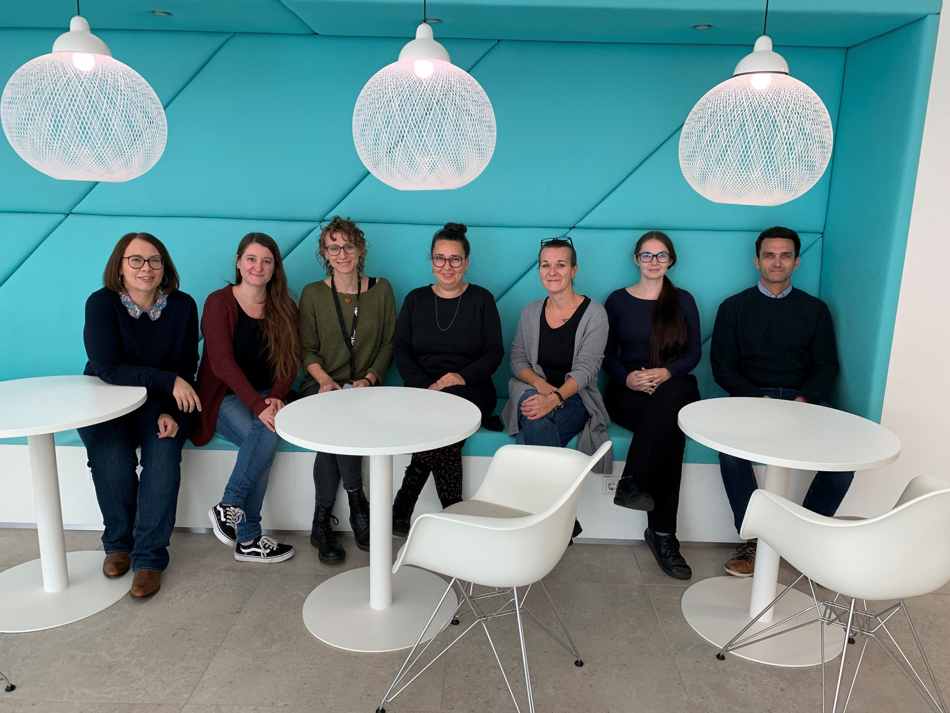 7 Personen sitzen auf einer Bank, davor stehen Tische und Stühle