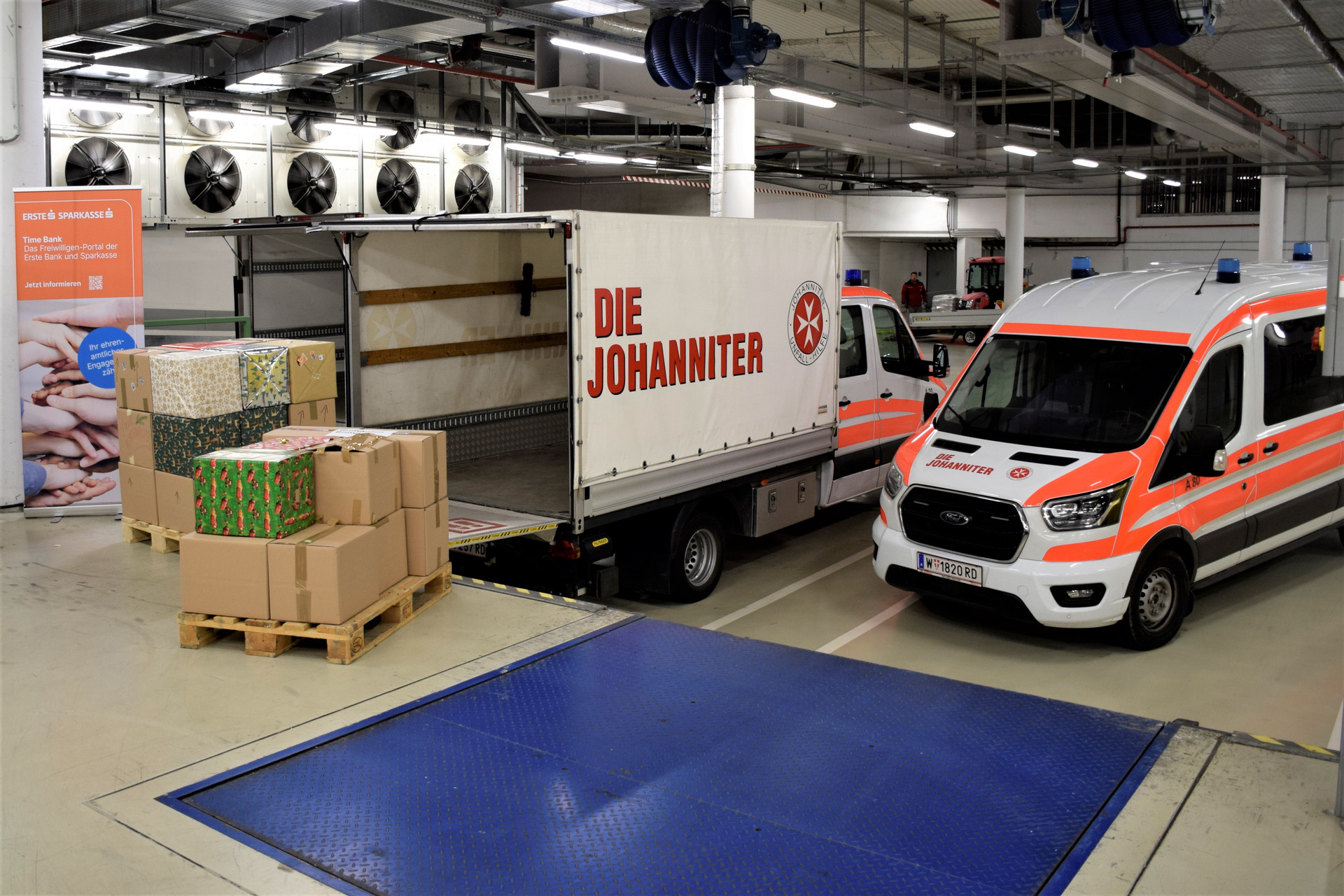 Aufgestapelte Hilfspakete neben zwei Johanniter-LKWs - bereit zum Einladen.